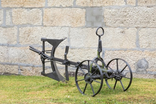 Old iron plow with wheels placed as garden ornament.