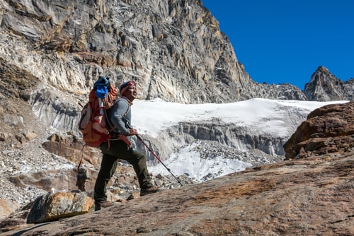 Iconic Portrait of Nepalese professional Mountain Guide staying on Rock and looking up at high Altitude Summits carrying Backpack with alpine climbing Gear.