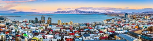 Aerial panorama of downtown Reykjavik at sunset with colorful houses and snowy mountains in the background.