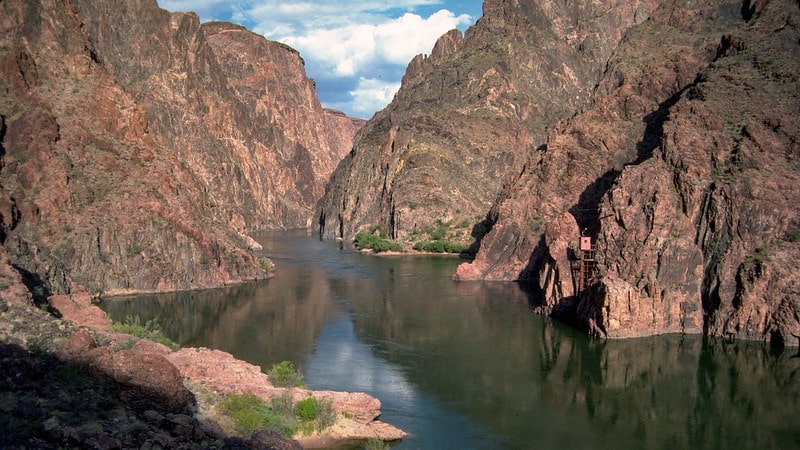 Colorado River view upriver from the black bridge, showing cliffs of the inner gorge on both sides of a calm river surface.